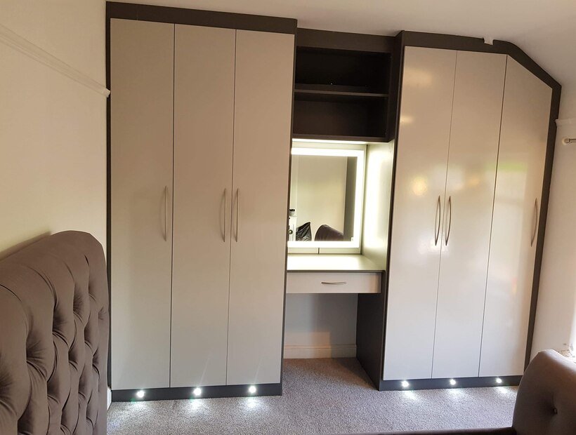 Bespoke cream fitted wardrobes with a built-in dressing table under a sloped ceiling in Warrington