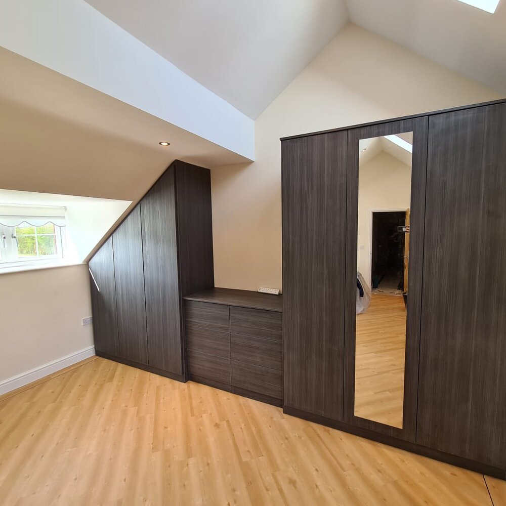 Fitted wardrobes shaped around an angled ceiling beside a window