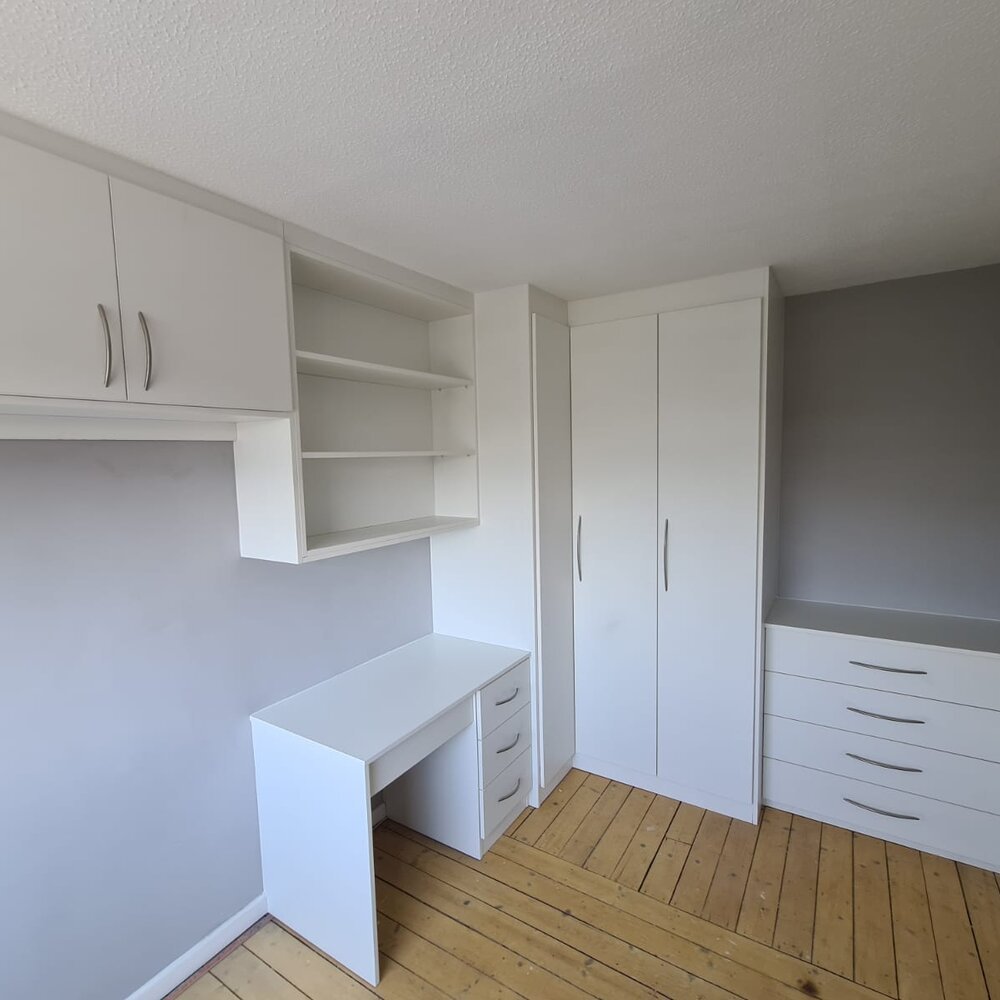White fitted wardrobe with a built-in desk and drawers under a low eaves in Warrington