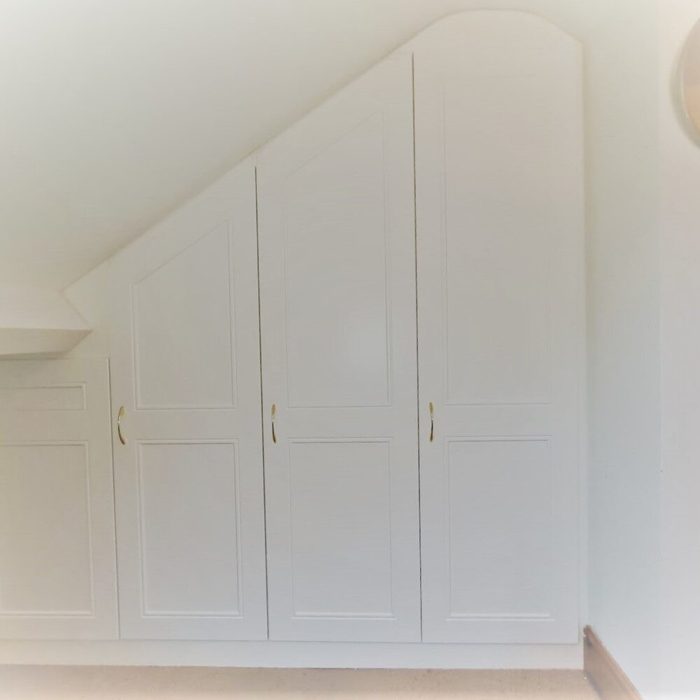 White fitted wardrobes built under the eaves of a bedroom