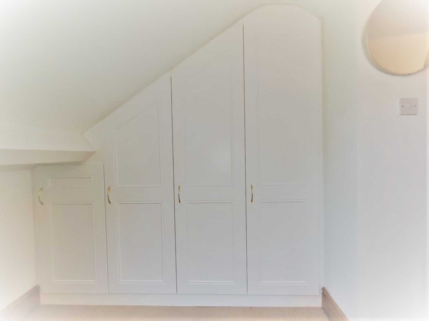 Made-to-measure fitted wardrobes following a sloped ceiling in a bright loft bedroom